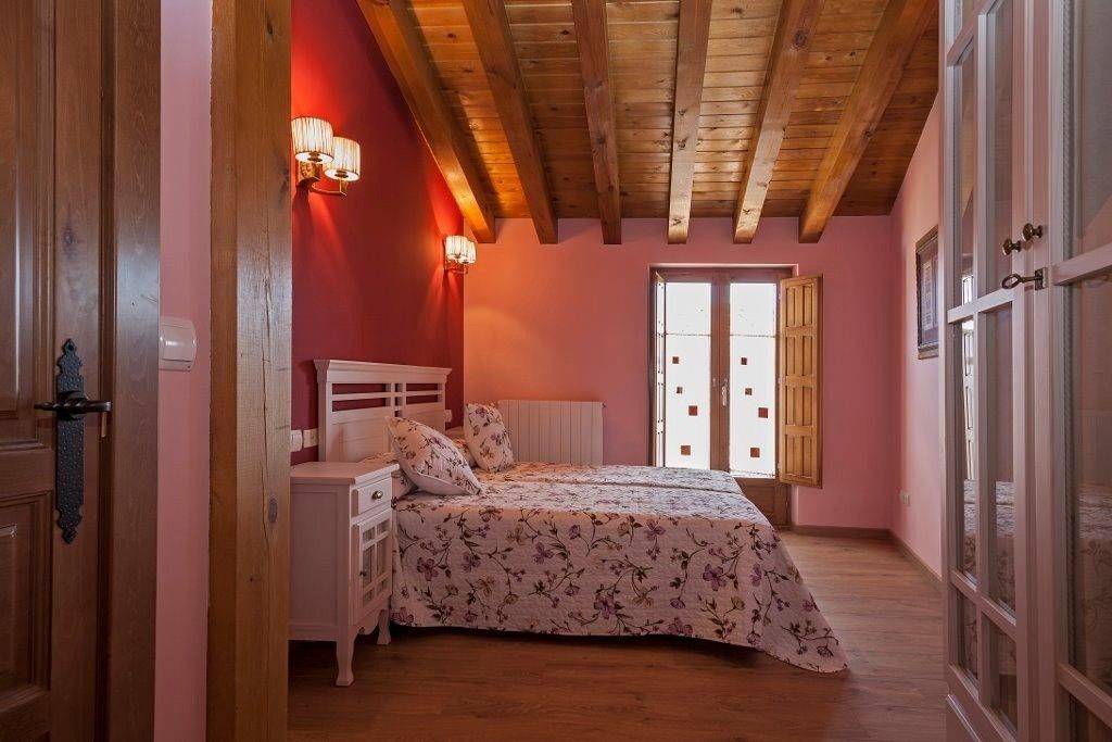 Un dormitorio con cama, paredes rosas, una pared decorativa roja, vigas de madera a la vista en el techo.