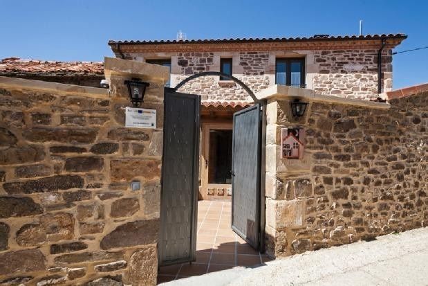 Un patio con muros de piedra y una puerta metálica abierta conduce a una casa rústica de piedra de dos plantas .