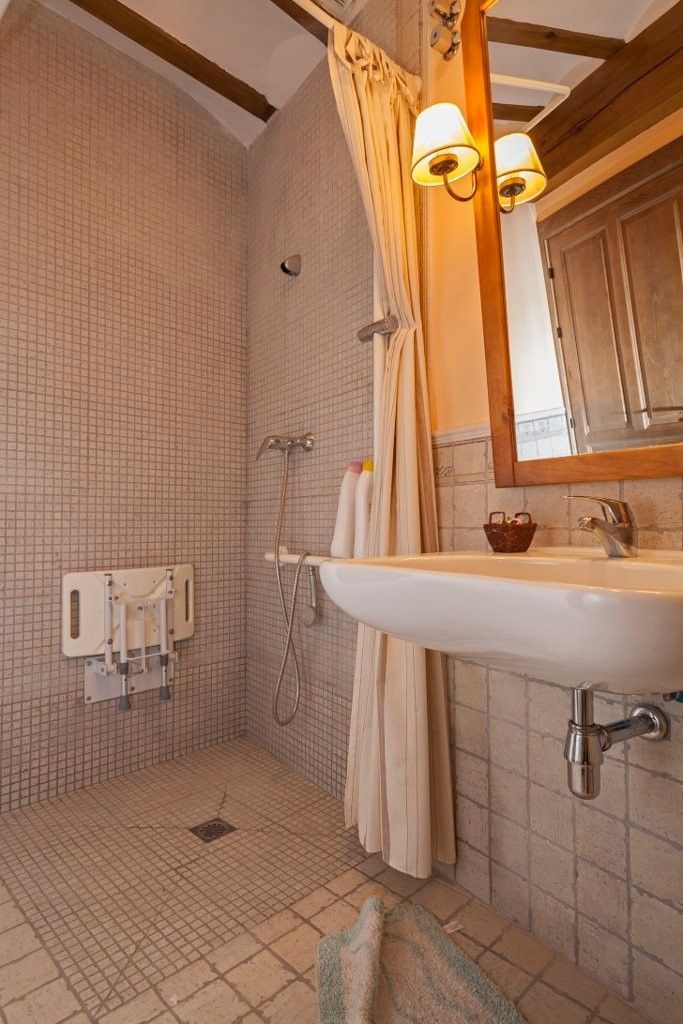 Un baño accesible en tonos neutros que cuenta con una ducha a ras de suelo con asiento abatible montado en la pared .