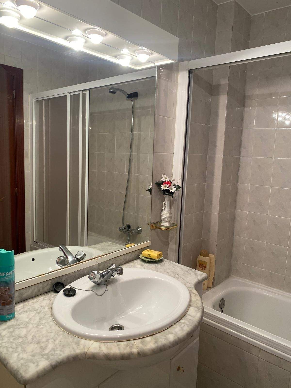 Un baño con tocador blanco con encimera estilo mármol, lavabo, espejo grande y bañera y ducha alicatadas.