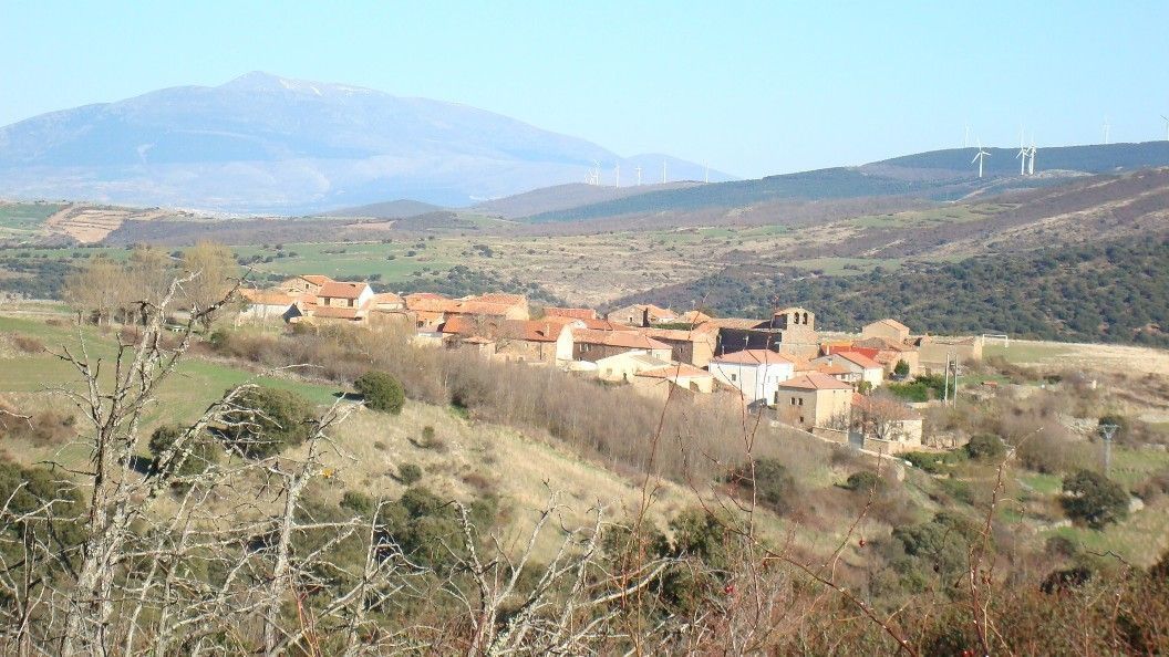 Un pequeño pueblo rústico con edificios de piedra con tejados de terracota, enclavado en un paisaje soleado y montañoso.