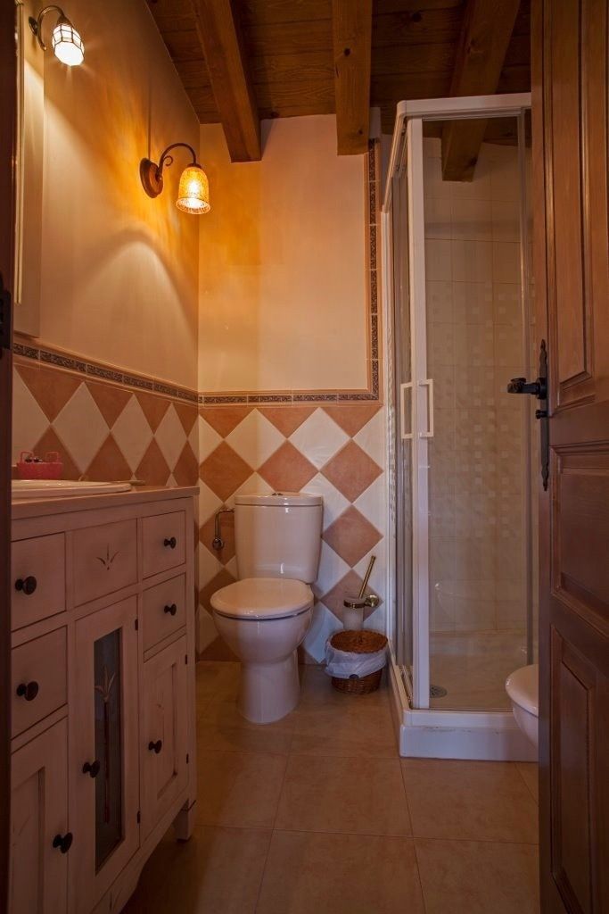 Un baño rústico con tocador de madera, inodoro, cabina de ducha de cristal e iluminación cálida.