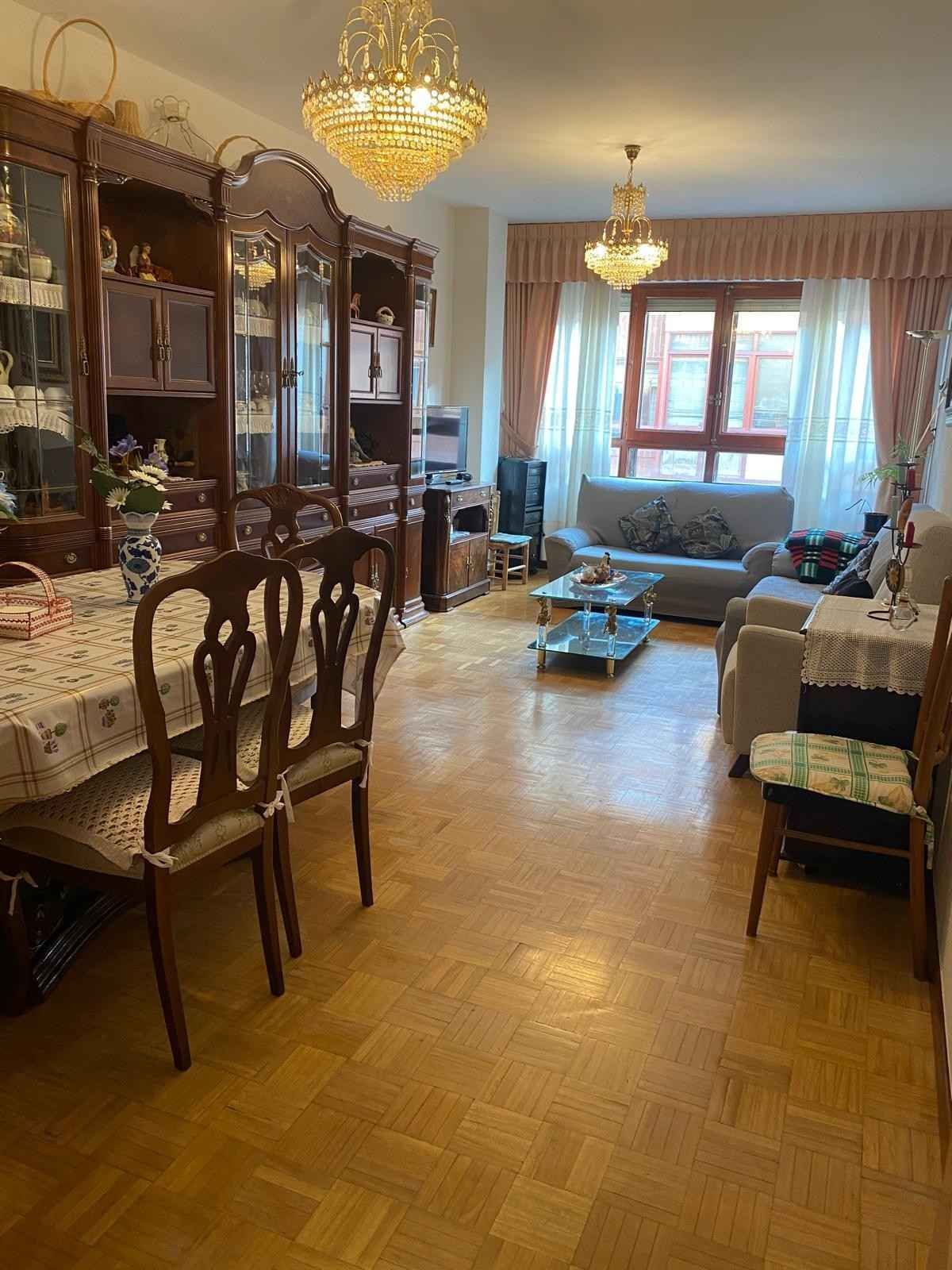 Un clásico salón-comedor con suelo de parqué de madera, lámparas de araña de cristal, una gran vitrina y un sofá.