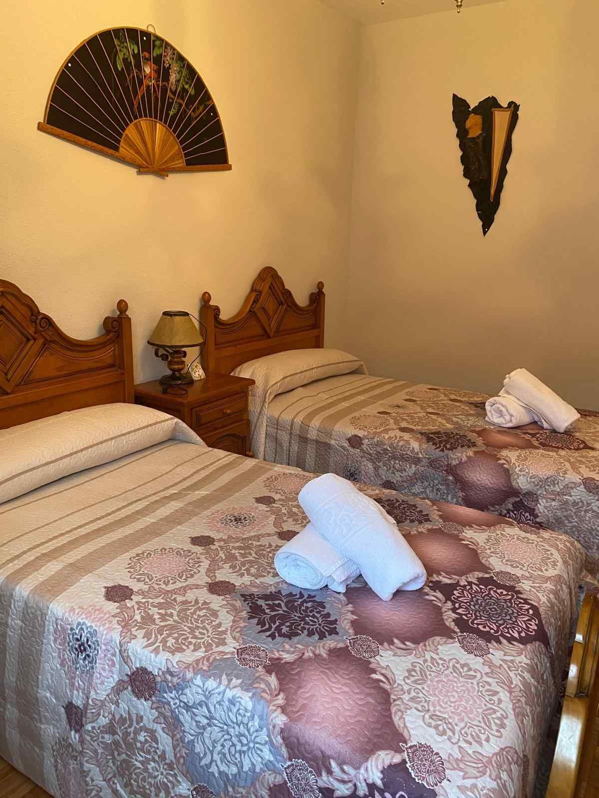 Dos camas individuales con mantas estampadas y toallas blancas en un dormitorio con cabeceros.