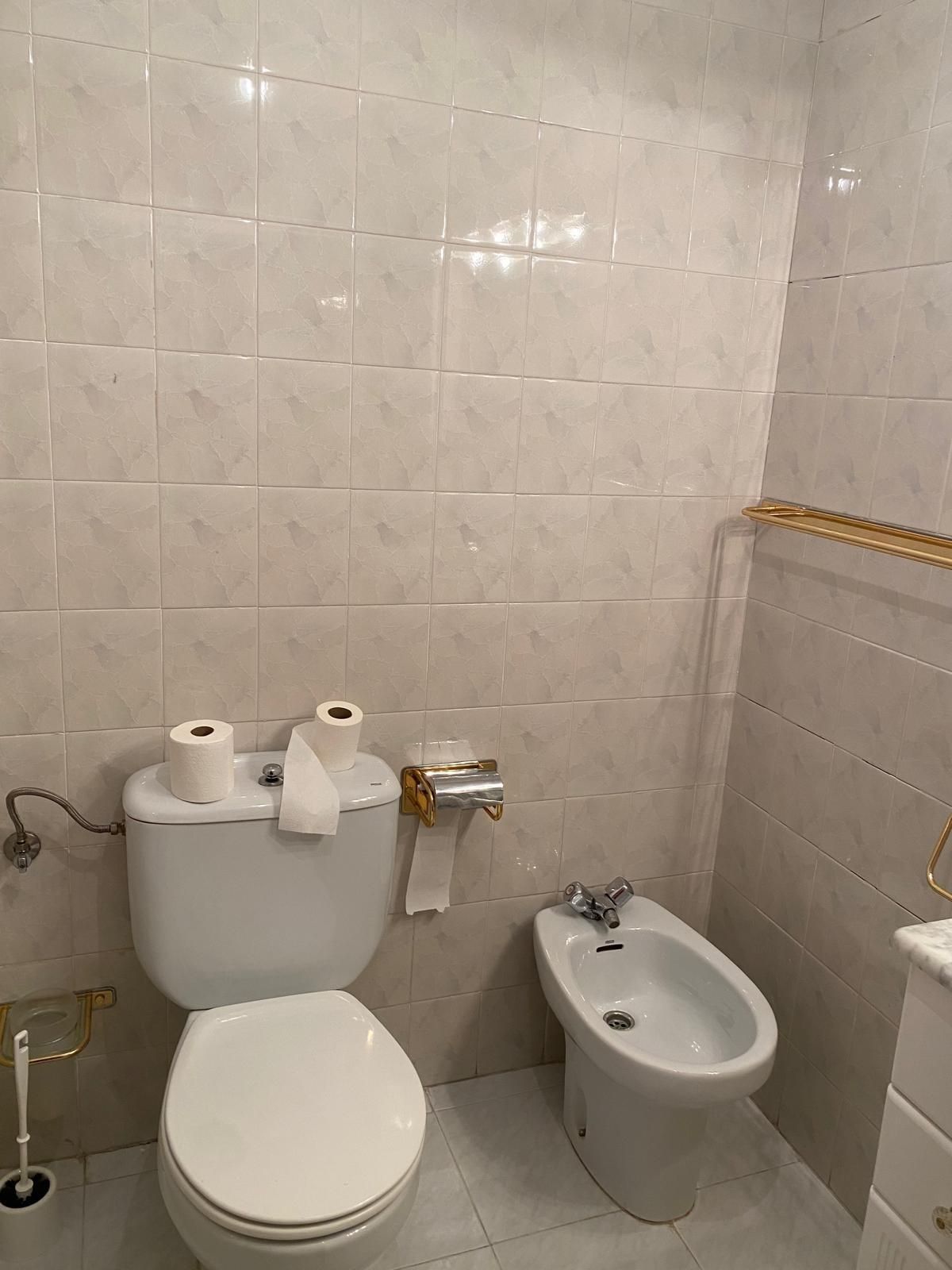 Un inodoro blanco y un bidé colocados uno al lado del otro en un baño con paredes y suelos de azulejos de color claro.