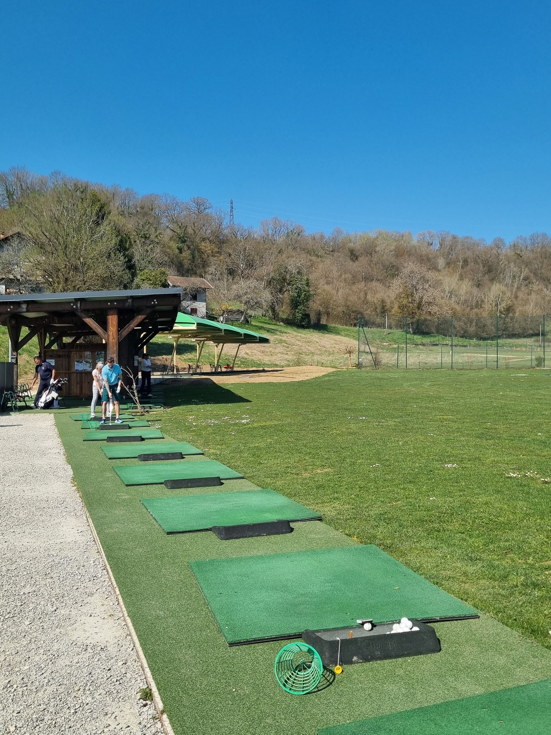 Terrain de minigolf avec tapis verts à côté d'un abri en bois sur un terrain herbeux ensoleillé.