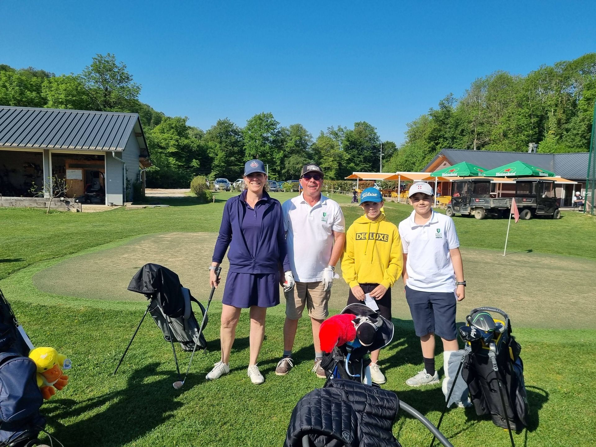 Des golfeurs posent avec leurs clubs sur un parcours de golf ensoleillé, près d'un club-house et de voiturettes.