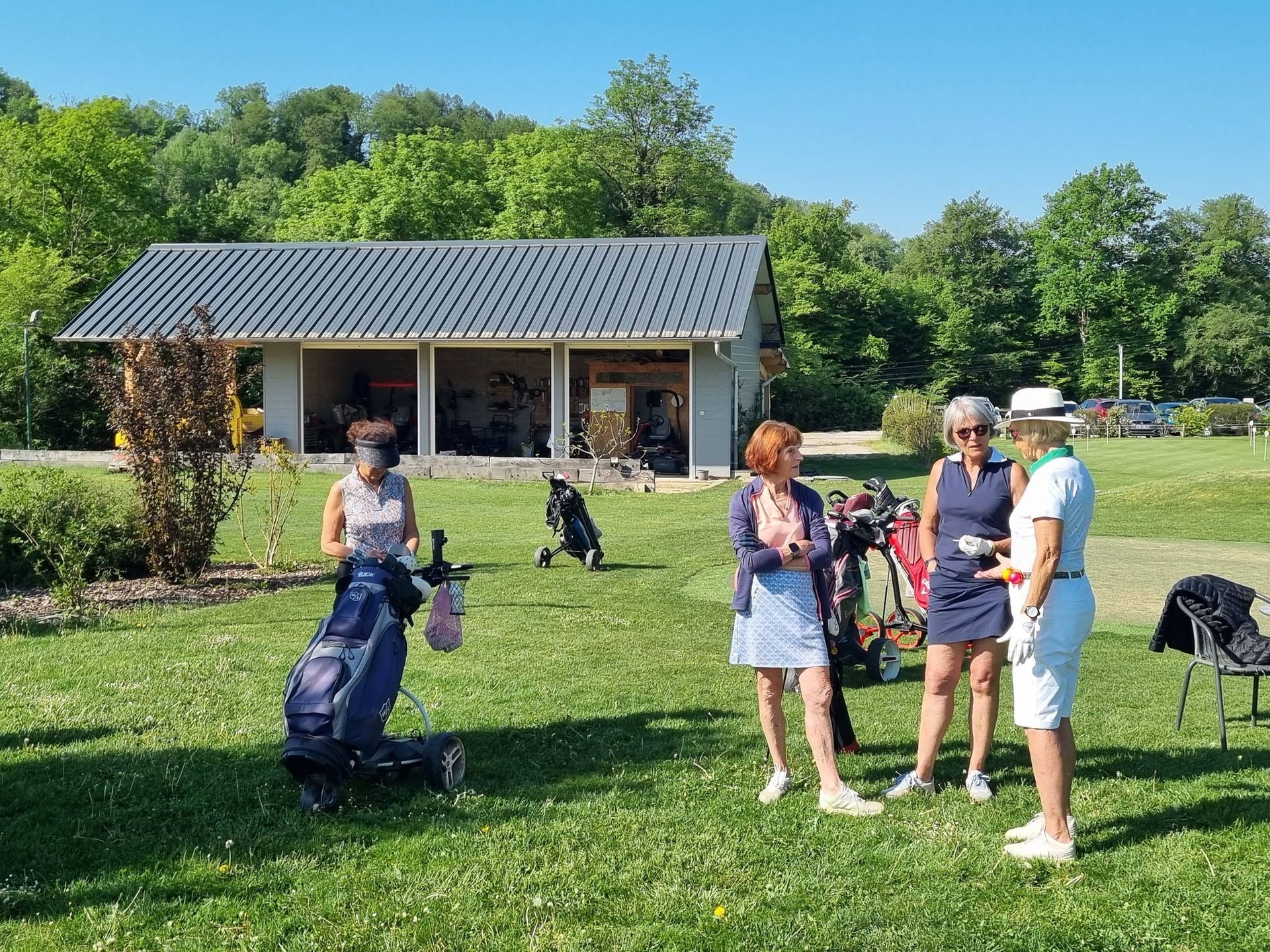 Des personnes se tiennent debout sur une pelouse près d'un petit bâtiment par une journée ensoleillée.