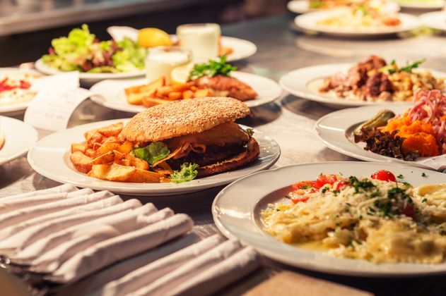Des plats gastronomiques dressés sur une table à manger, comprenant un sandwich et un risotto crémeux, avec des serviettes pliées devant.