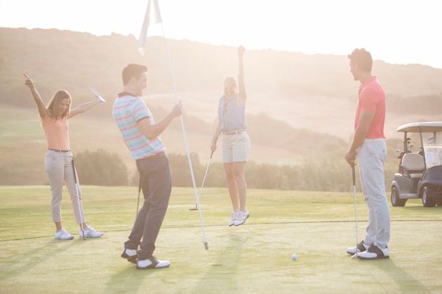 Des amis jouent au golf sur un parcours ensoleillé au coucher du soleil avec une voiturette de golf en arrière-plan.