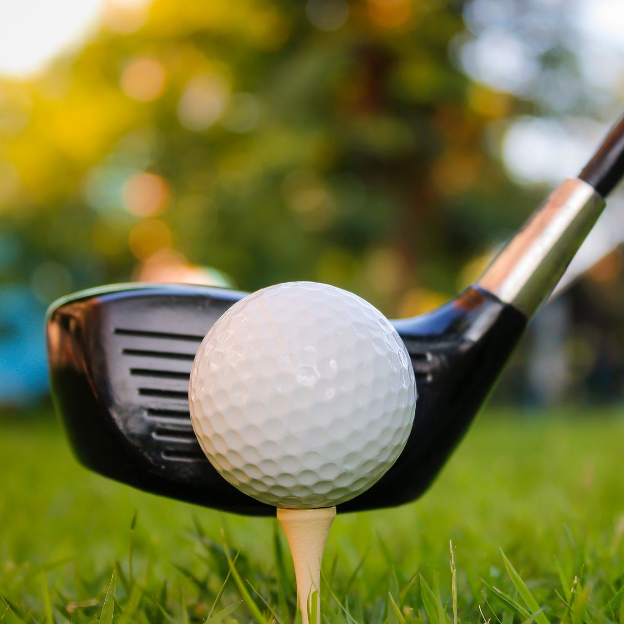 Balle de golf sur un tee avec un club prêt derrière, sur un parcours herbeux.