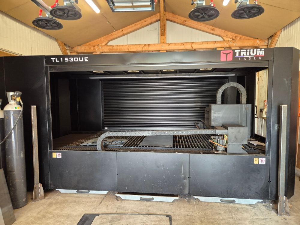 Grande machine de découpe laser industrielle noire dans un atelier avec poutres apparentes au plafond et éclairage zénithal