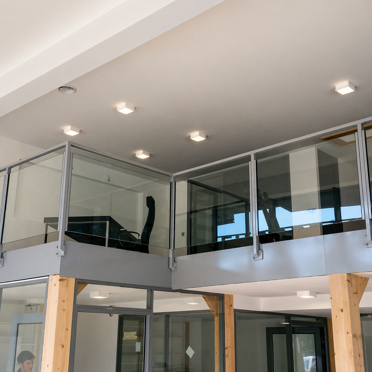 Intérieur de loft moderne avec mezzanine à balustrade en verre, poutres en bois et éclairage encastré au plafond
