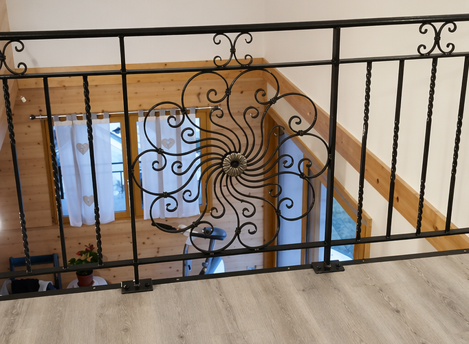 Rambarde d'escalier en fer forgé noir donnant sur une cage d'escalier lumineuse aux murs blancs et aux marches en bois