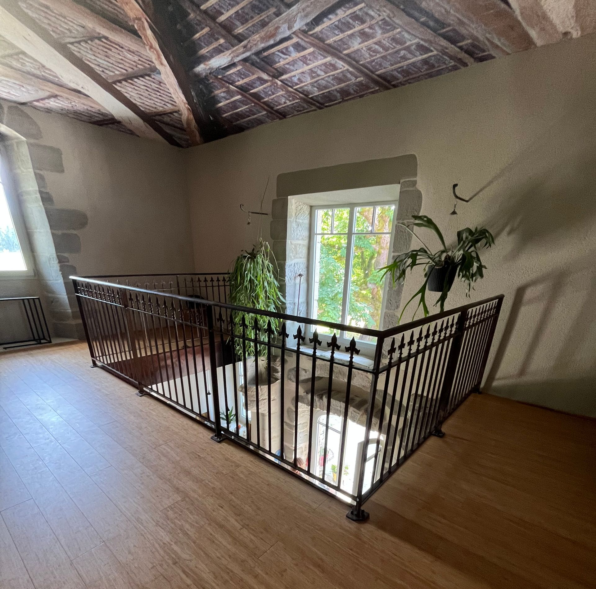 Couloir à l'étage avec parquet, rampe en fer forgé et fenêtre éclairée par la verdure extérieure