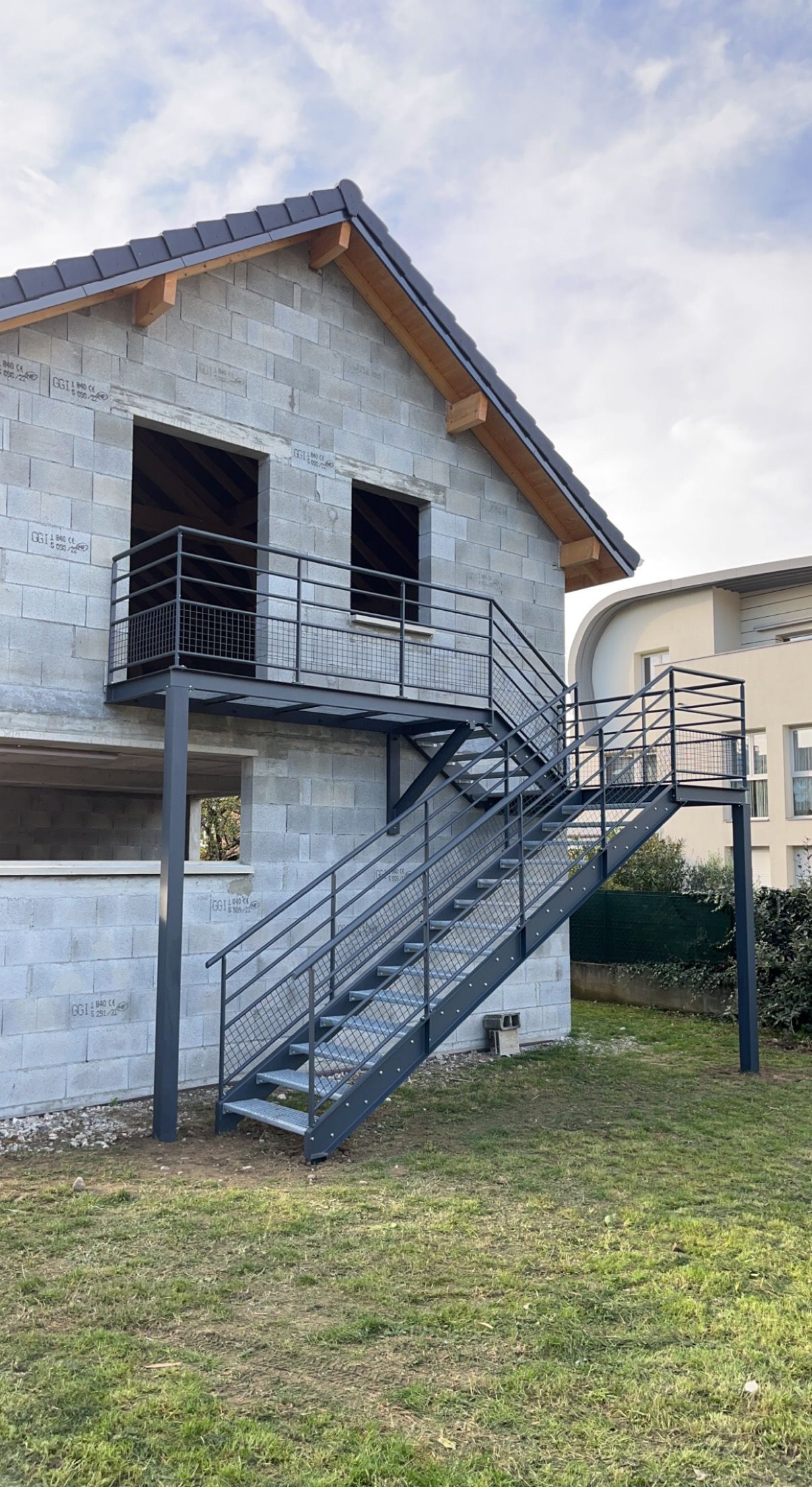 Maison blanche de deux étages avec escalier extérieur en métal et petit balcon sur un terrain gazonné