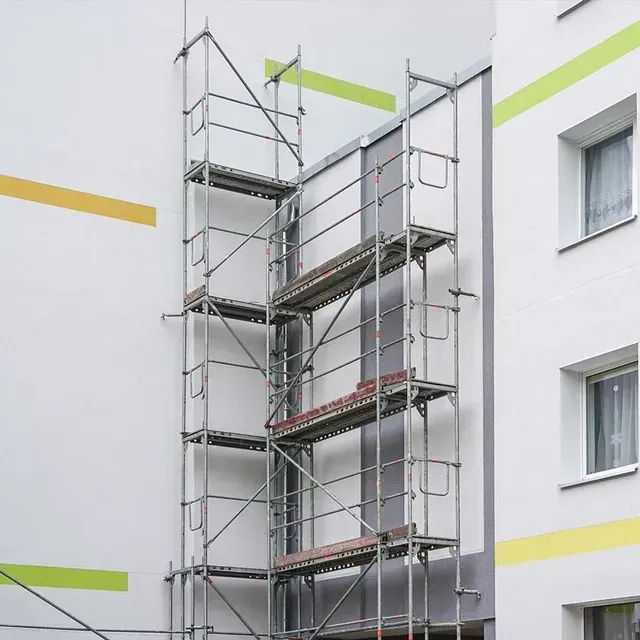 Andamios adosados a un edificio blanco con ventanas grises y franjas decorativas de color verde lima y amarillo.