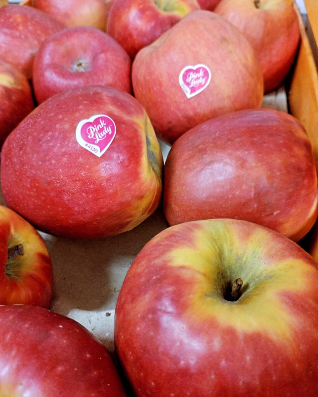 Primer plano de un grupo de manzanas Pink Lady en una caja. Las manzanas son rojas y tienen una pegatina en forma de corazón.