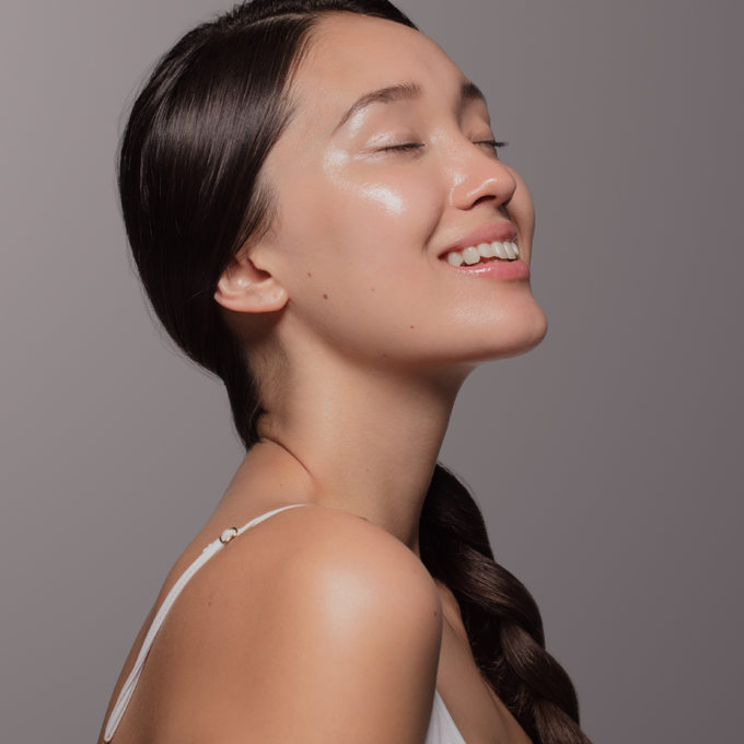 Una mujer sonríe con los ojos cerrados y el cabello recogido en una trenza.