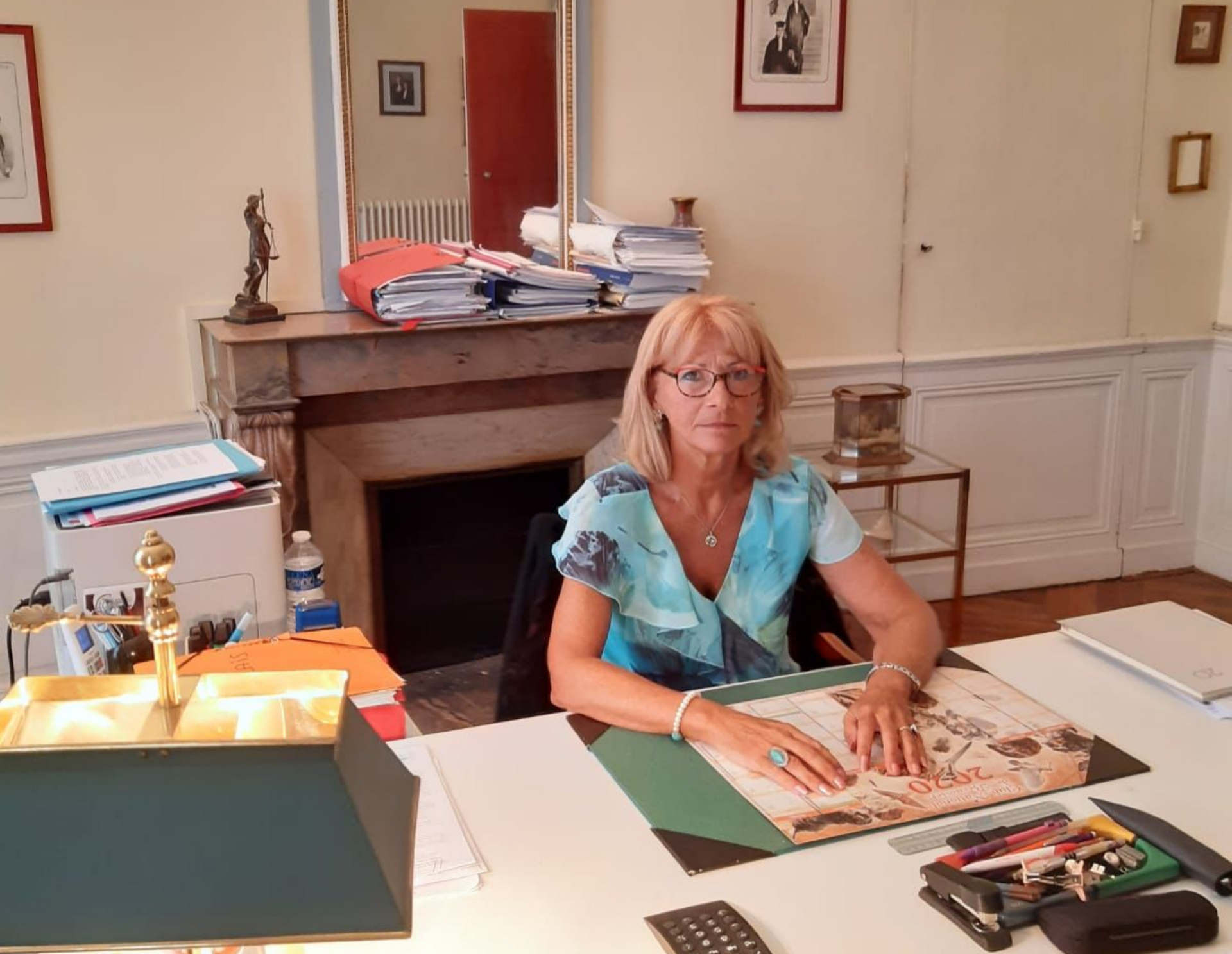 Maître LE FLOCH-CHAPLAIS assise à son bureau, des papiers empilés derrière elle, regarde l'objectif.