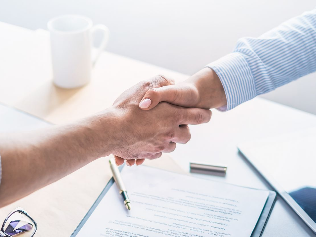 Deux personnes se serrent la main au-dessus d'un contrat posé sur un bureau.
