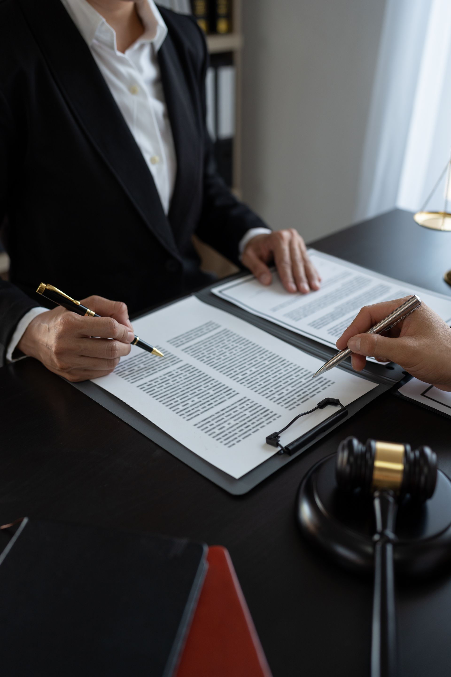 Deux personnes examinent des documents à un bureau ; un maillet et une balance se trouvent sur le bureau.