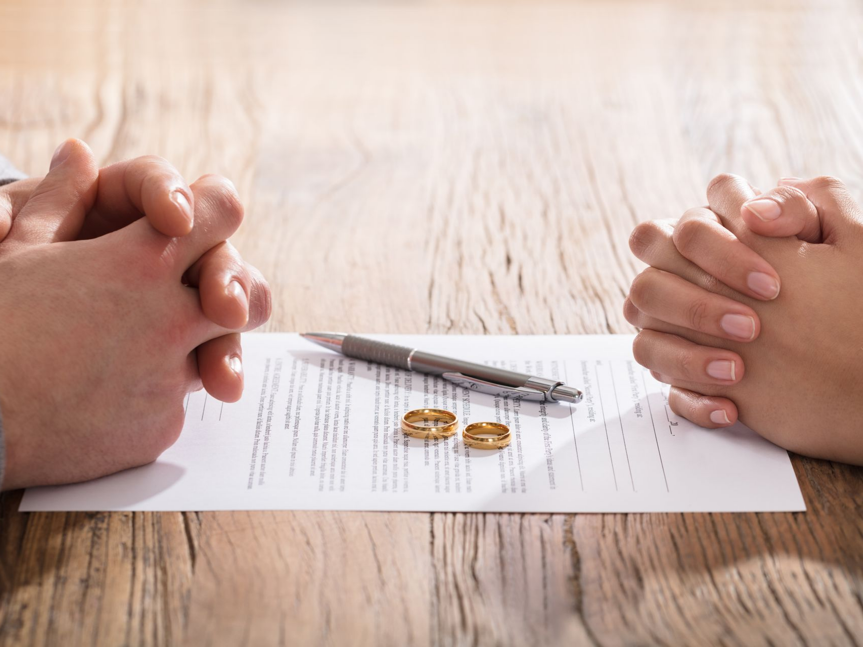 Des mains jointes sur un accord de divorce ; des alliances et un stylo reposent sur le papier.