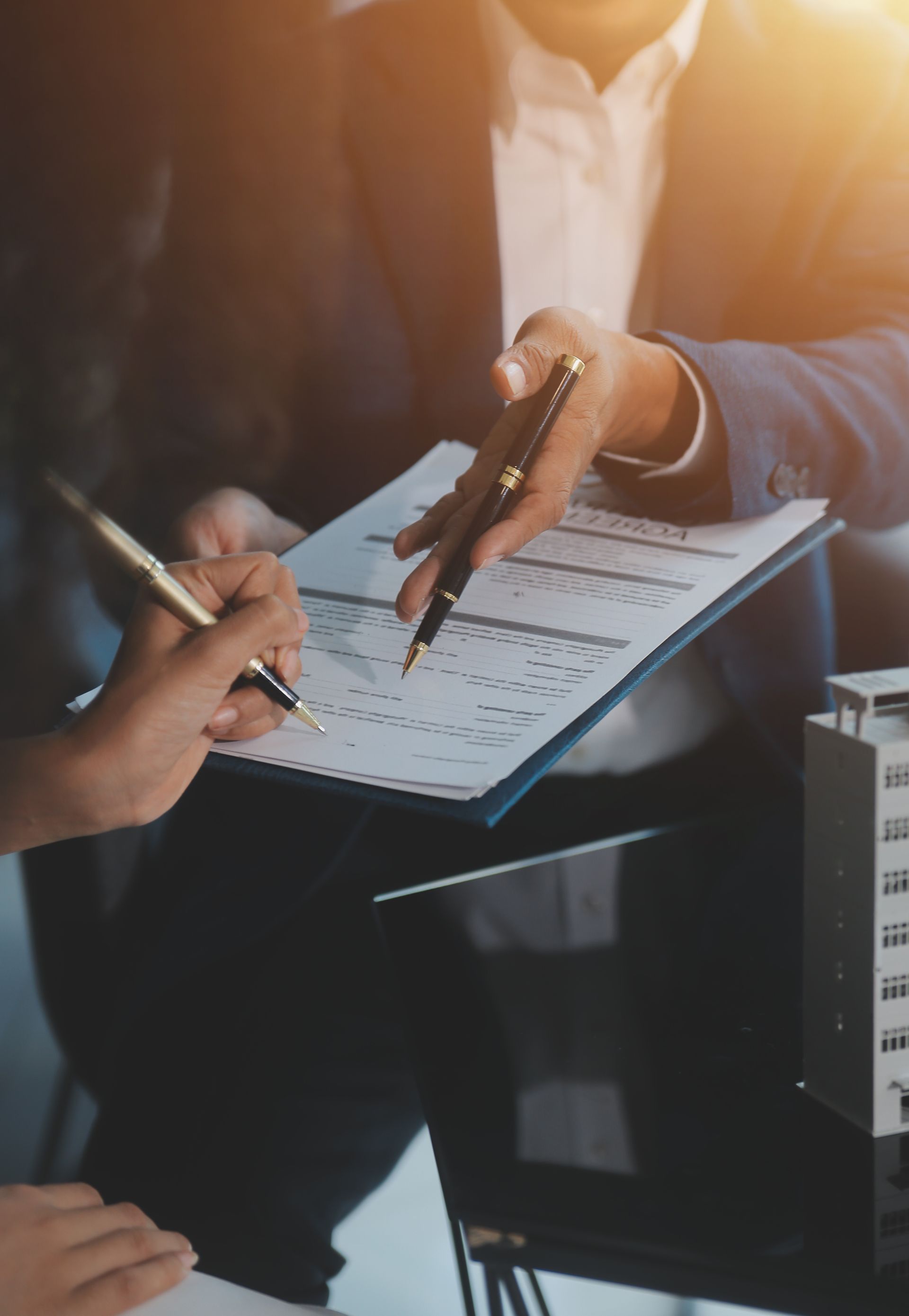Deux personnes signent le document, l'une d'elles le désigne avec un stylo.
