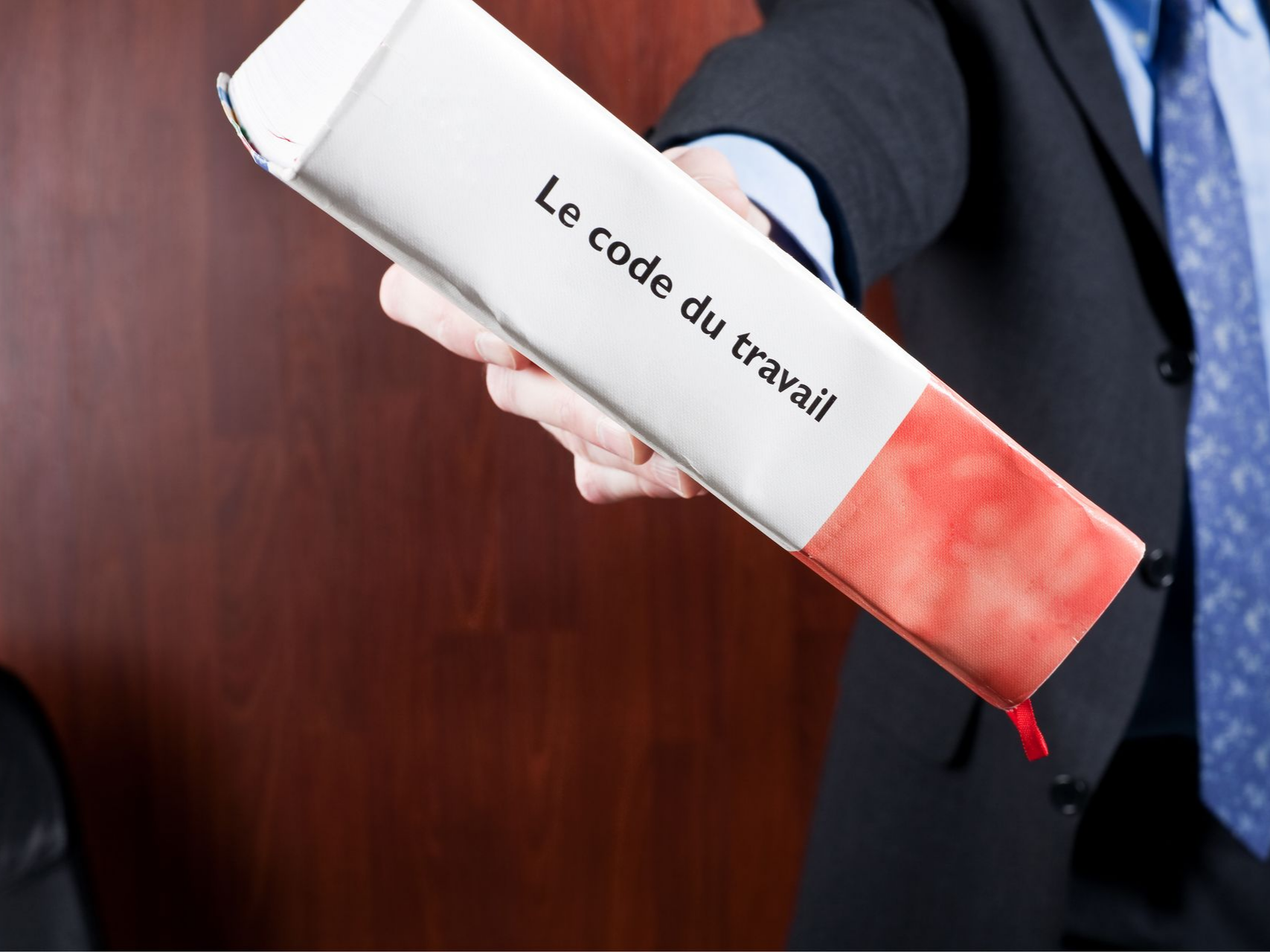 Personne en costume tenant un classeur où est écrit Le Code du travail.