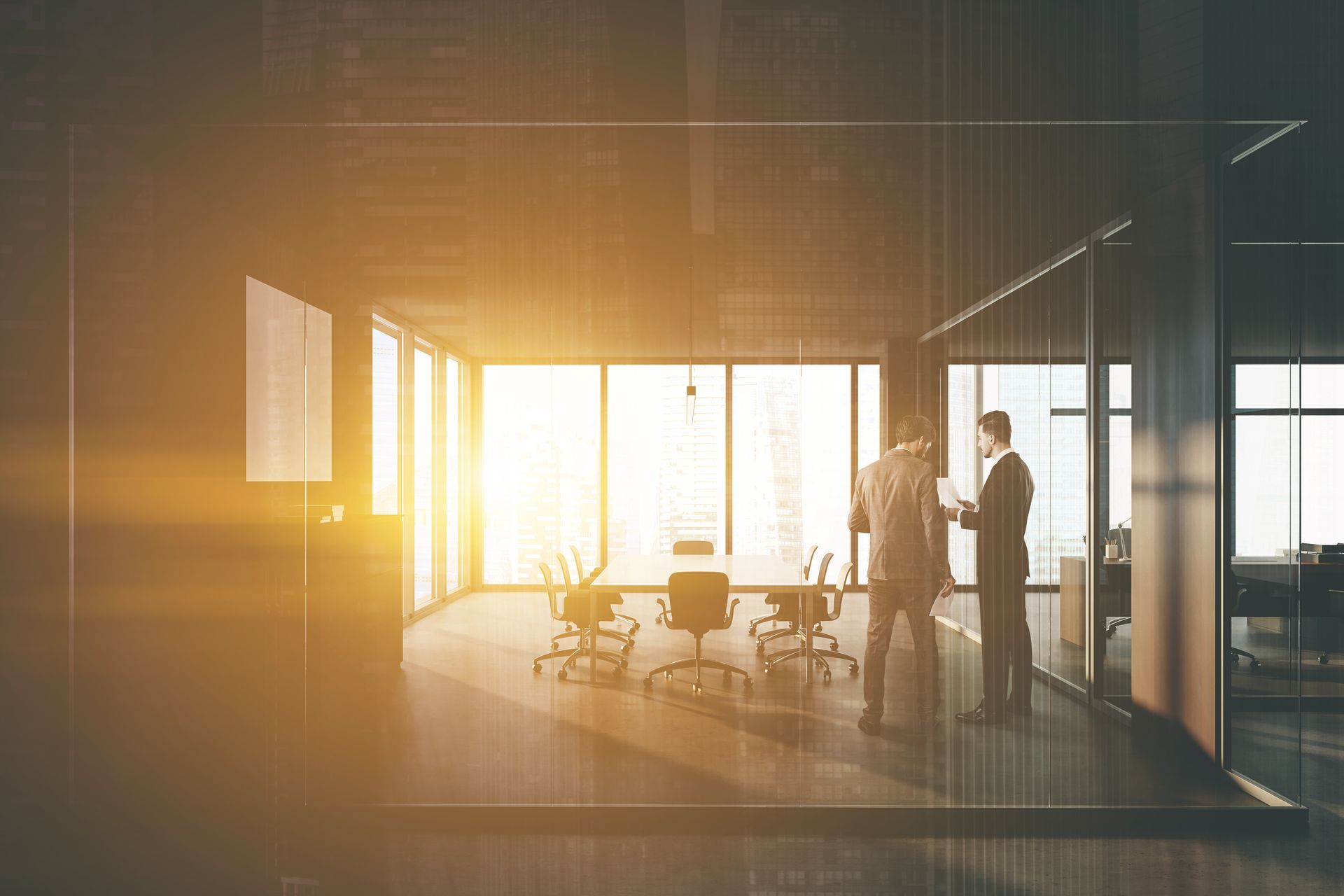 Deux personnes en costume se tiennent dans un bureau moderne avec de grandes fenêtres donnant sur la ville, en train de discuter.