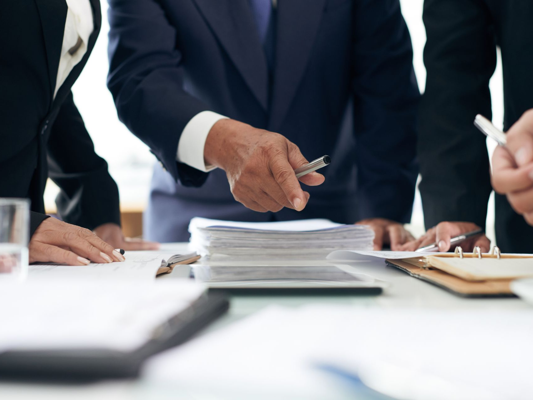 Des hommes d'affaires examinent des documents autour d'une table. L'un d'eux désigne les papiers du doigt avec un stylo.