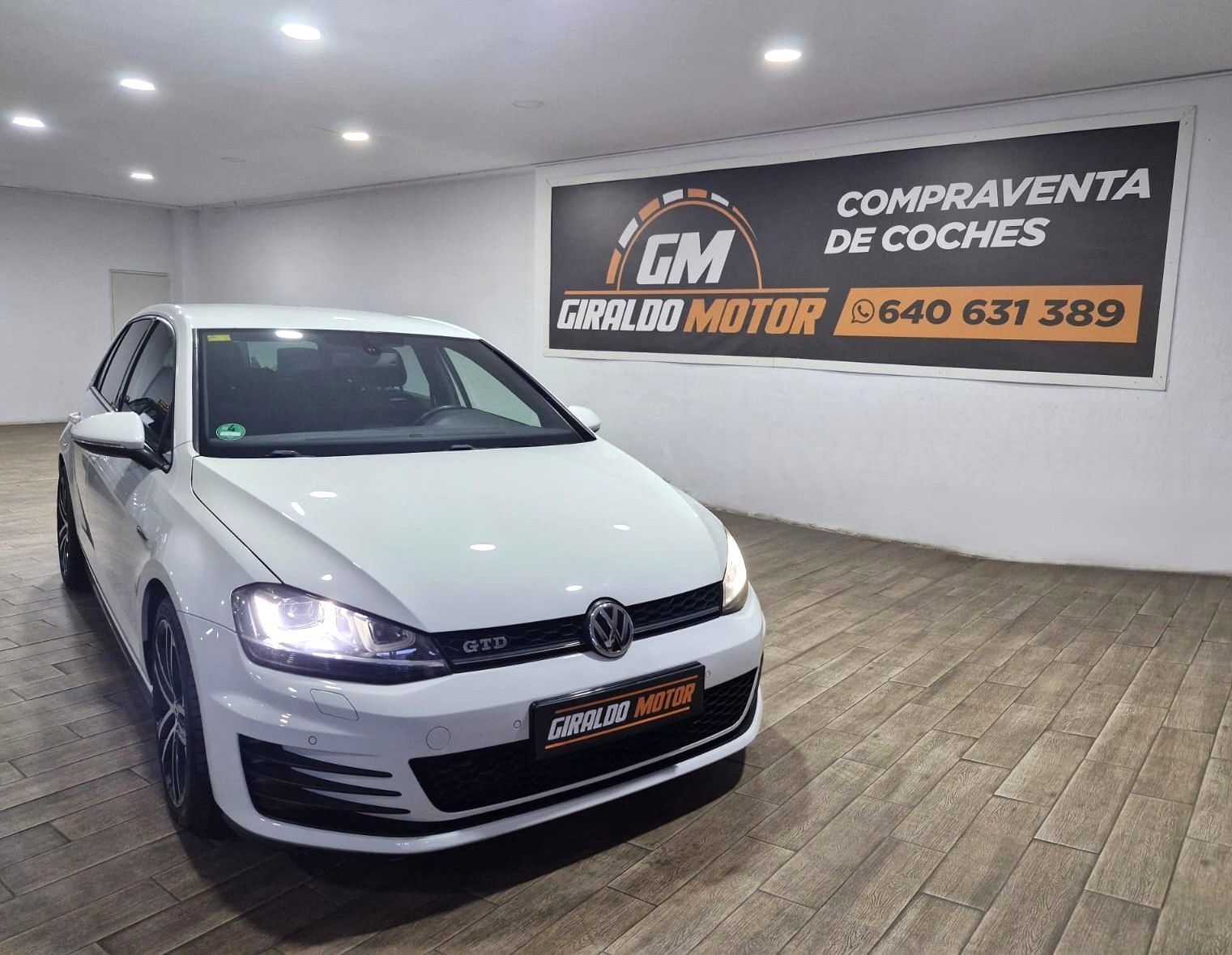 Coche Volkswagen Golf blanco en una sala de exposición con un cartel de "Compraventa de Coches".