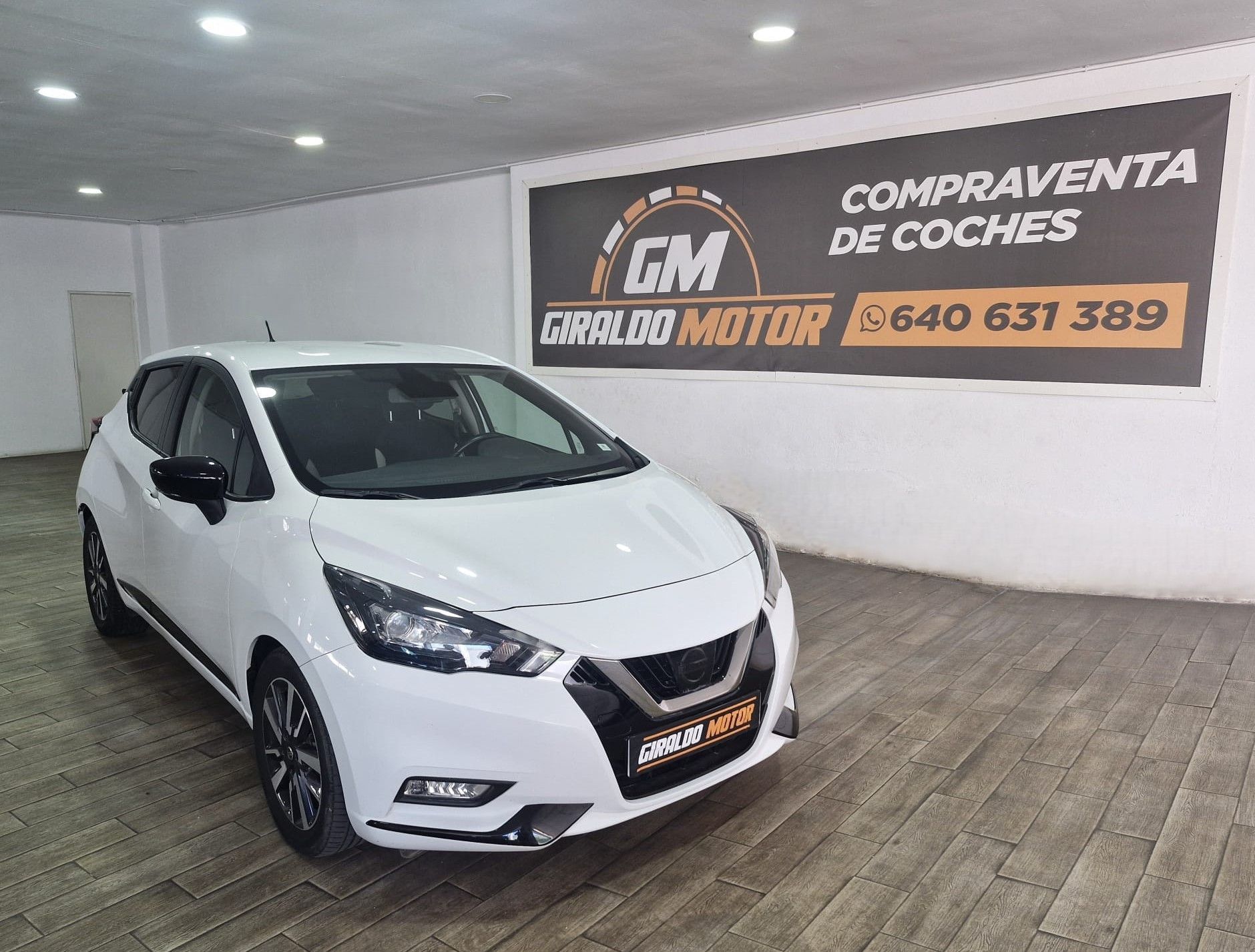 Nissan Micra blanco en un concesionario de automóviles con cartel "GM Giraldo Motor".
