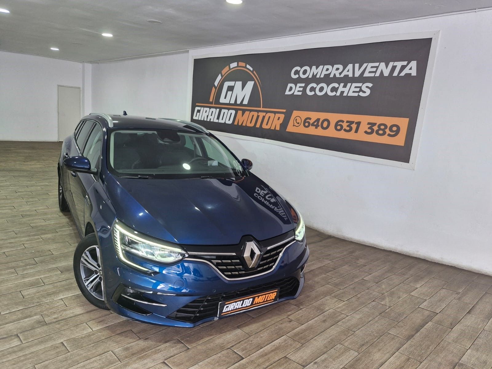 Renault Mégane familiar de color azul en un concesionario con el cartel "COMPRAVENTA DE COCHES".
