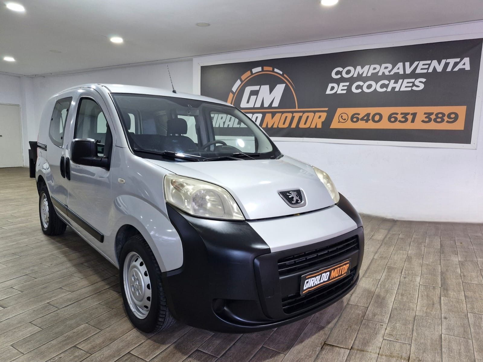 Furgoneta Peugeot Bipper de color plata estacionada en el interior de un concesionario de automóviles.