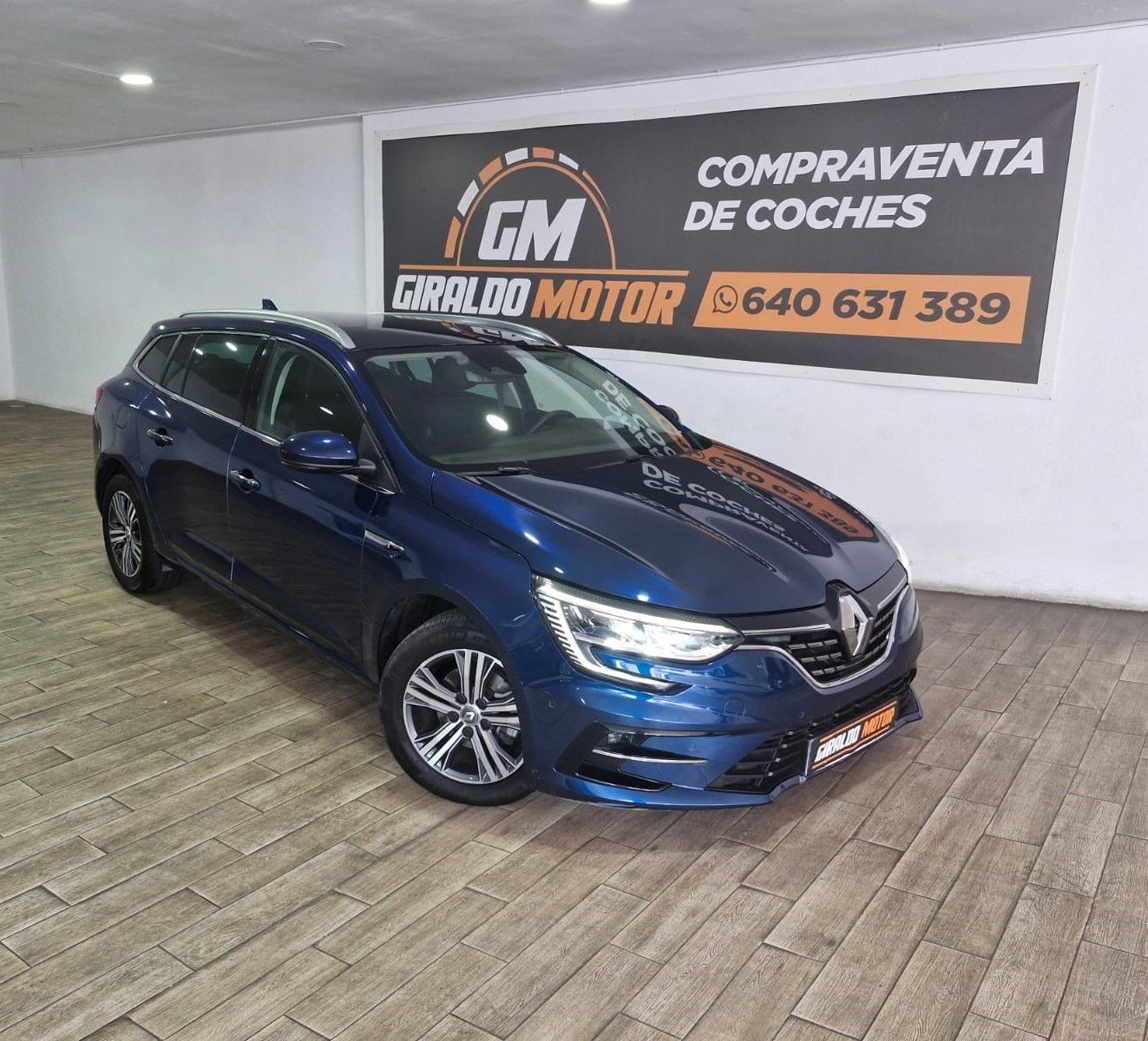 Un automóvil Renault Mégane de color azul en un concesionario; al fondo hay un cartel de Giraldo Motor.