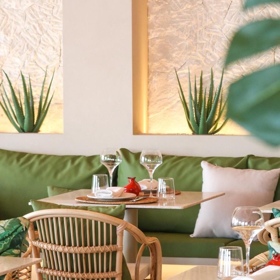 Una mesa de restaurante preparada para cenar con cojines verdes y plantas de aloe en nichos de pared.