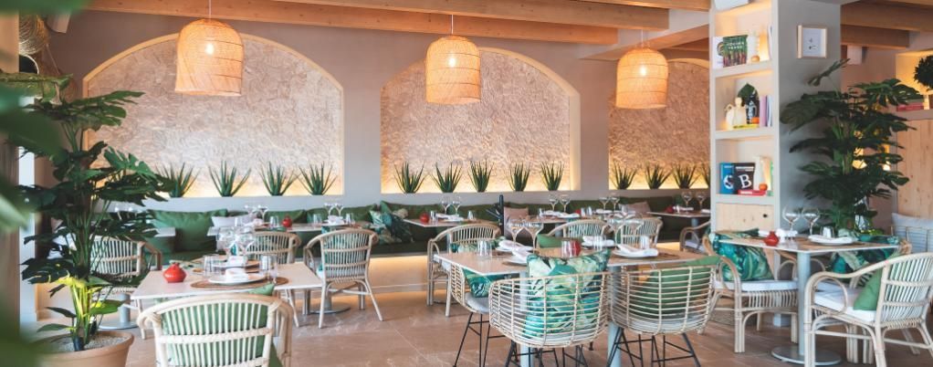 Interior de restaurante con decoración de paredes arqueadas, lámparas de ratán y mesas con detalles verdes.