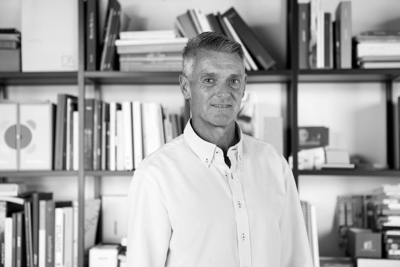 Hombre con camisa blanca sonriendo delante de una estantería llena de libros.
