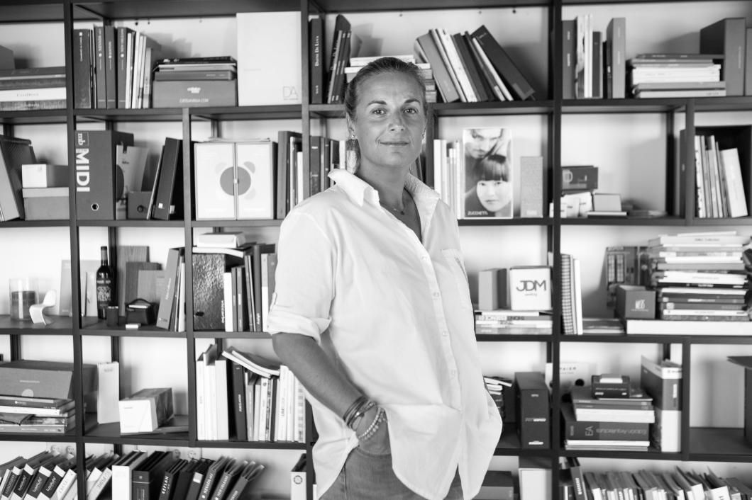 Una mujer con camisa blanca está parada frente a una estantería llena de libros y archivos.