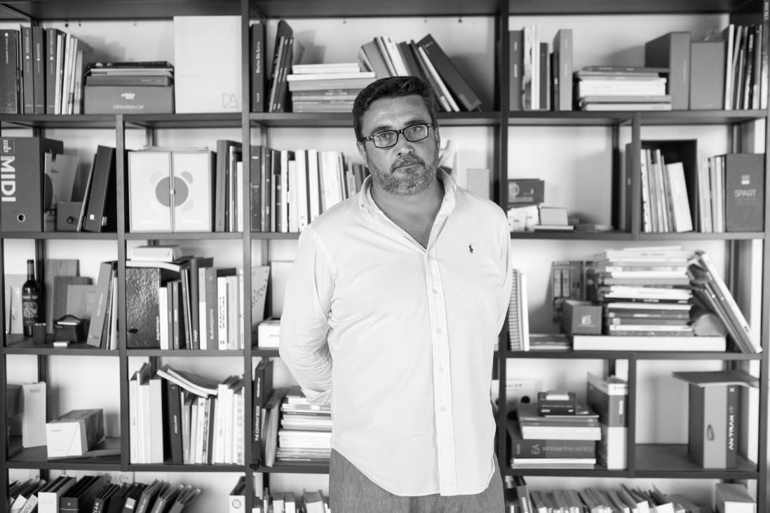 Un hombre con gafas se encuentra frente a una estantería llena de libros, con las manos tras la espalda 