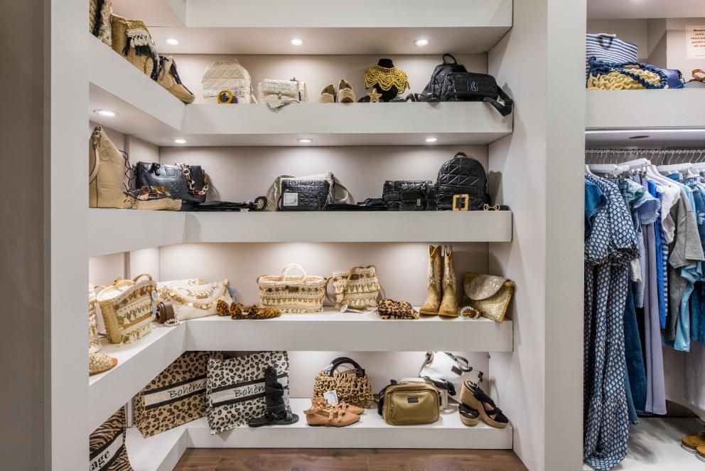 Estanterías empotradas en armario que muestran bolsos, zapatos y accesorios de diseñador; en tonos neutros y bien iluminados.