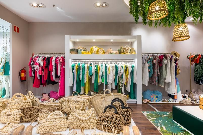 Interior de una tienda de ropa con estantes con prendas coloridas y bolsos tejidos en exhibición.
