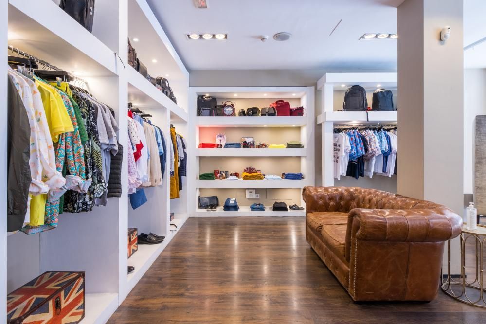 Interior de tienda de ropa con percheros, estanterías empotradas, sofá de cuero y suelo de madera.