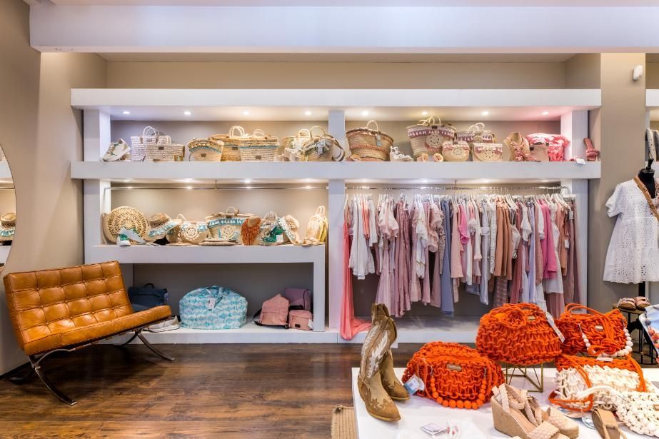 Interior de una boutique de ropa con mercancía en estantes y percheros, además de una silla de cuero naranja.