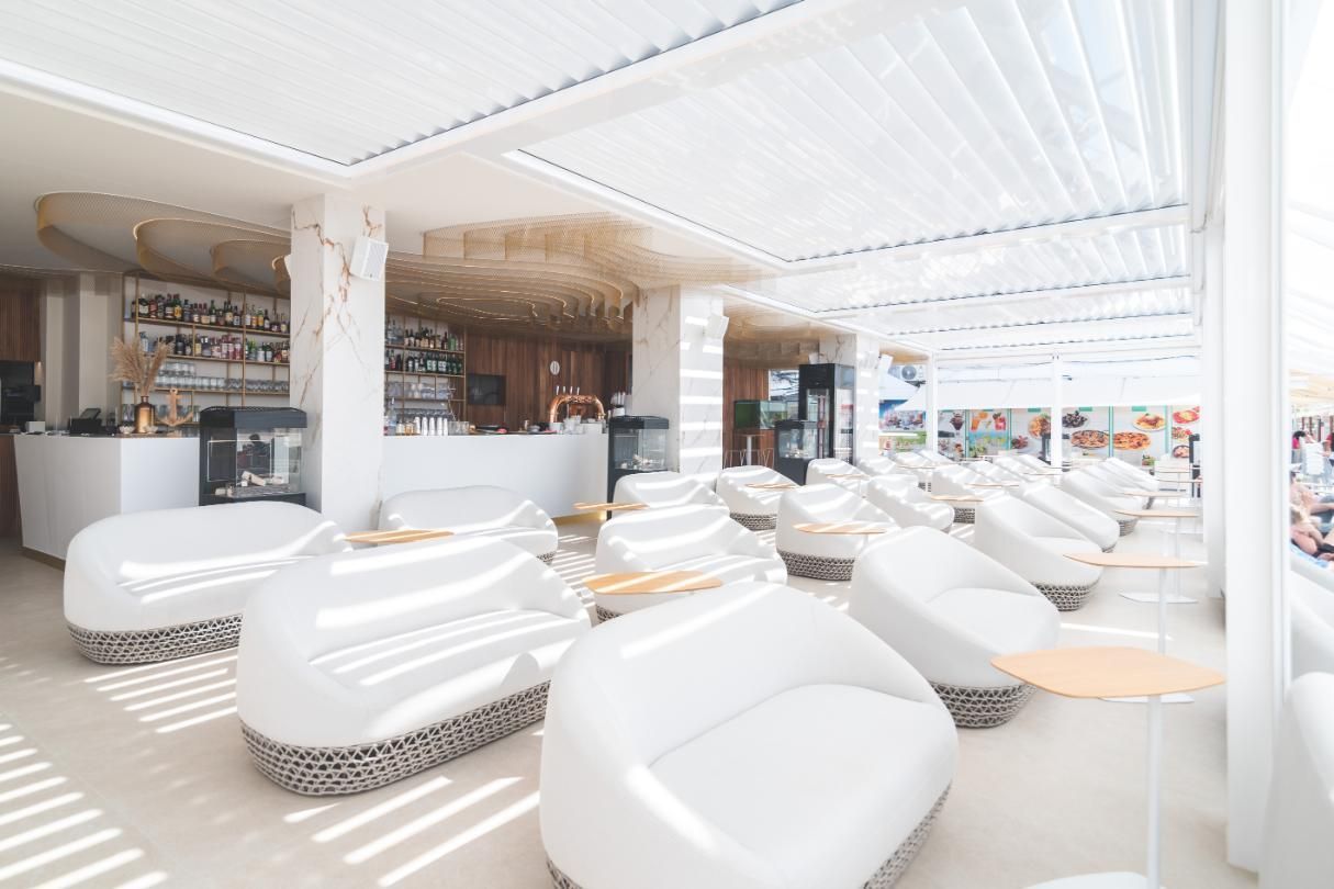 Salón exterior blanco con asientos curvos y bar.