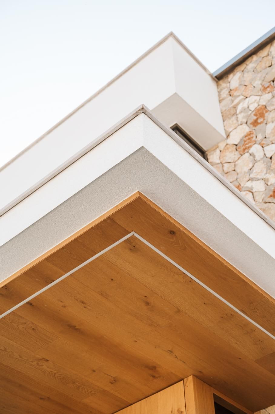 Esquina de un edificio moderno con paneles de madera, paredes blancas y fachada de piedra.