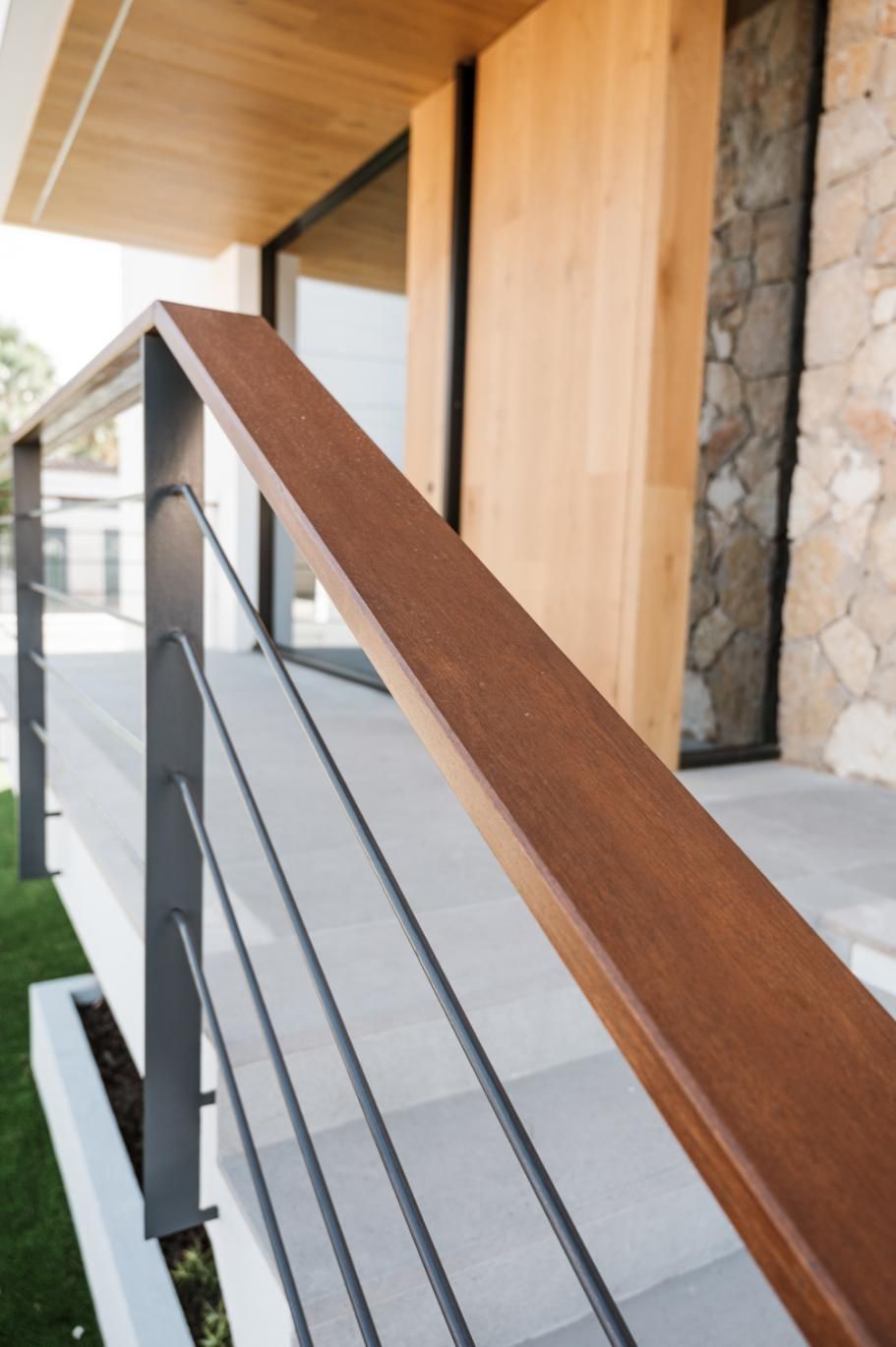 Pasamanos de madera con soportes metálicos de color gris y cables horizontales frente a una casa moderna.