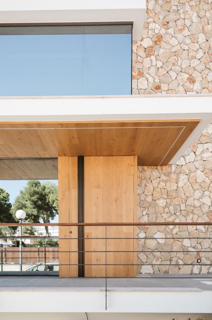 Fachada de edificio moderno con detalles en piedra y madera. Gran puerta de madera y balcón.