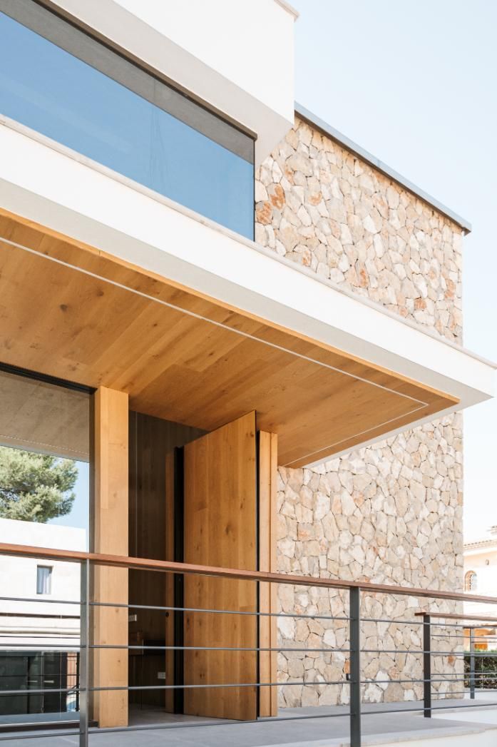 Edificio moderno con fachada de piedra, puerta de madera bajo un alero de madera y una ventana de cristal.